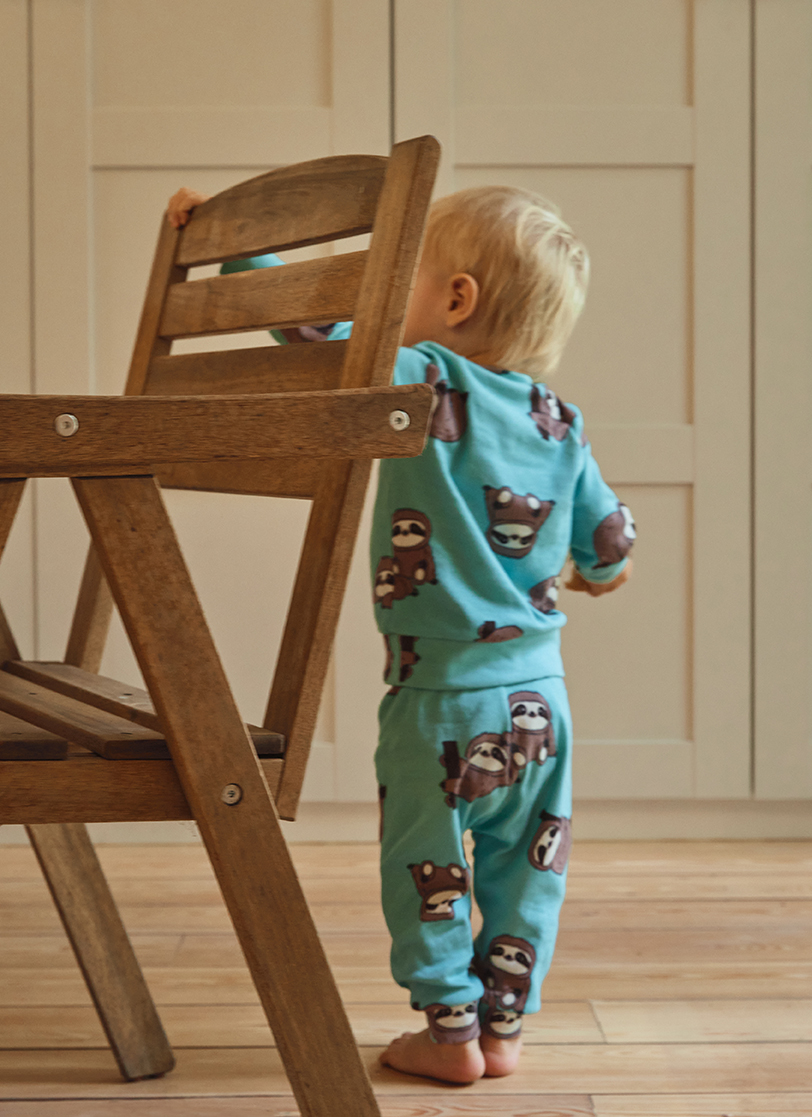 Dječak beba stoji pored stolice u plavoj pidžami sa motivom lemura