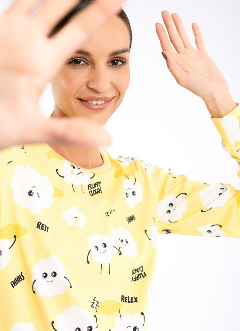 Žena stoji u pidžami žute boje sa motivima oblaka